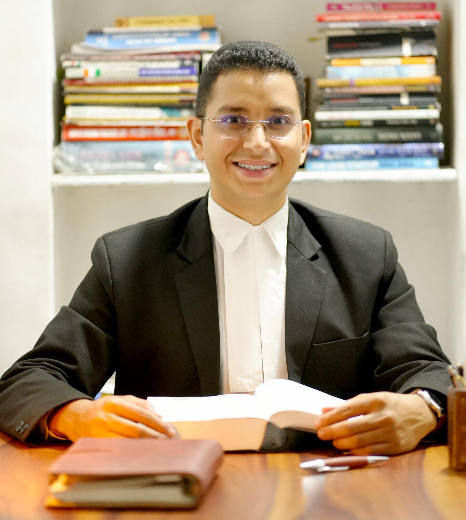 Advocate Ankit Chamoli smiling at desk with open law book and bookshelf